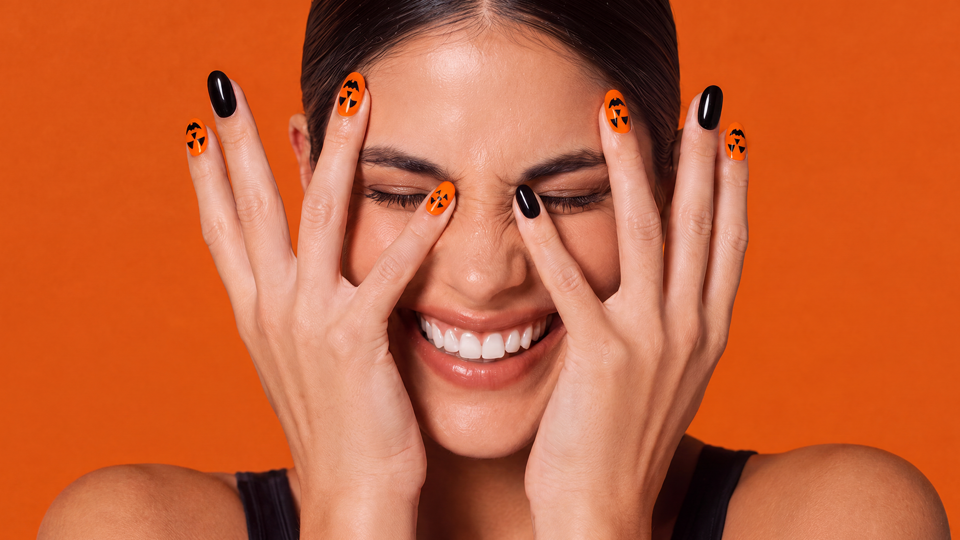 Glossy orange and black oval nails with playful jack-o’-lantern faces, perfect for a cute and spooky Halloween manicure.